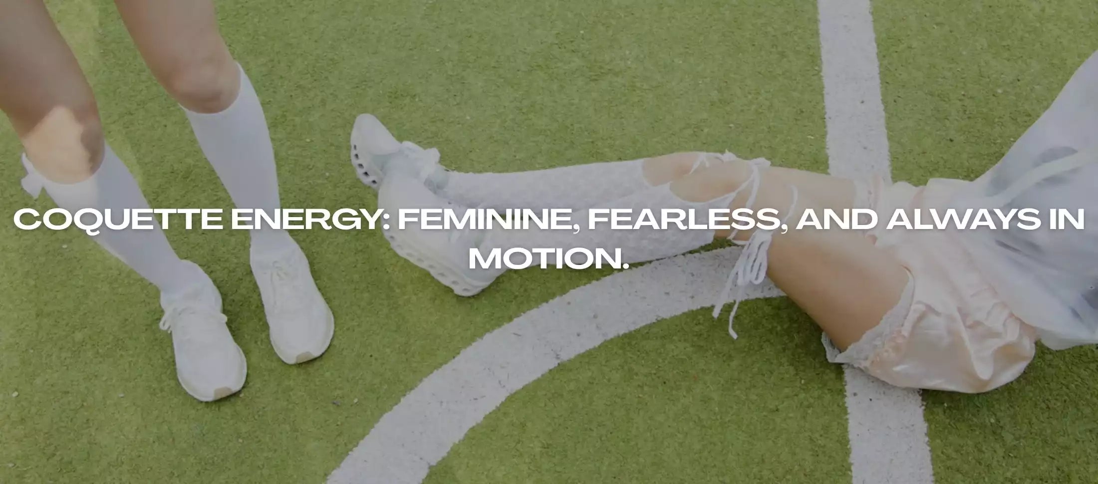Two women in coquette-inspired outfits with white sneakers and lace socks, sitting on a sports field – aesthetic fashion photography